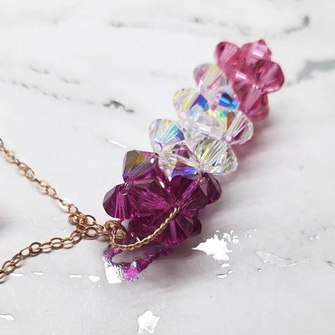 The 14 K Rose Gold Fill Super Sparkly Mom Crystal Pillar Pendant Necklace by Alexa Martha Designs features shimmering crystals on a rose gold chain, beautifully displayed on a white marble surface.