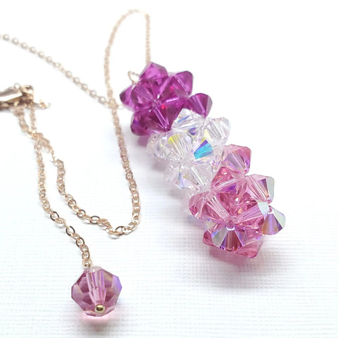 The 14K Rose Gold Fill Super Sparkly Mom Crystal Pillar Pendant Necklace by Alexa Martha Designs, featuring Swarovski crystals in pink, purple, and clear arranged from dark to light, shines beautifully on a white background.