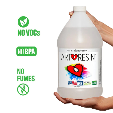 Someone holds the 2 Gal (7.57 L) ArtResin - Epoxy Resin bottle. Green icons show: No VOCs, No BPA, and No Fumes. The ArtResin label with a colorful heart and flags highlights its non-toxic, crystal-clear finish every time.