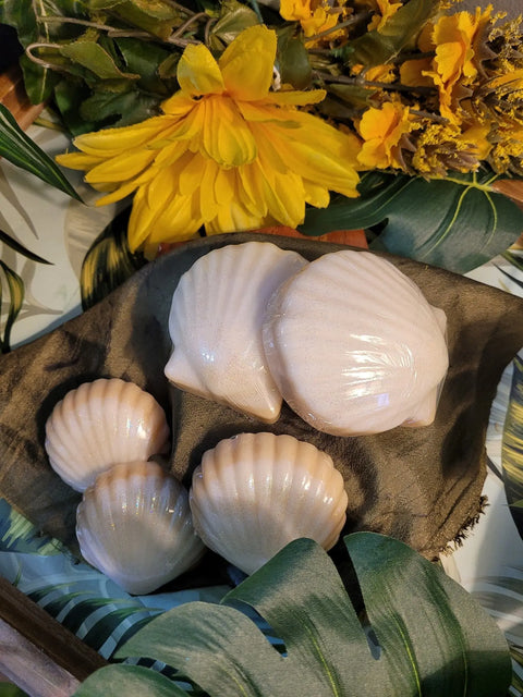 Shiny, seashell-shaped Bathsheba Body Works Moisture Bar - Bahama Sun soaps rest on a brown cloth amid tropical leaves and yellow flowers, providing a lotion alternative with a delightful tropical scent.