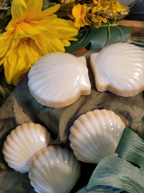 Four white, seashell-shaped Bathsheba Body Works Moisture Bar - Bahama Sun soaps sit on a dark green cloth with yellow artificial flowers and leaves—offering a perfect tropical scent as a lotion alternative.