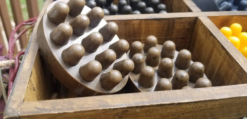 Two round brown massage tools with multiple knobs rest in a wooden divided box. Bathsheba Body Works Curly Hair Shampoo and other massage tools are partially visible in adjacent sections.