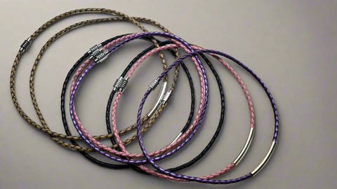 Five Alexa Martha Designs 3mm Bolo Leather Snap Off Chokers in black, brown, purple, and pink are displayed in overlapping circles on a gray surface. Some feature silver or metallic details and magnetic closures.