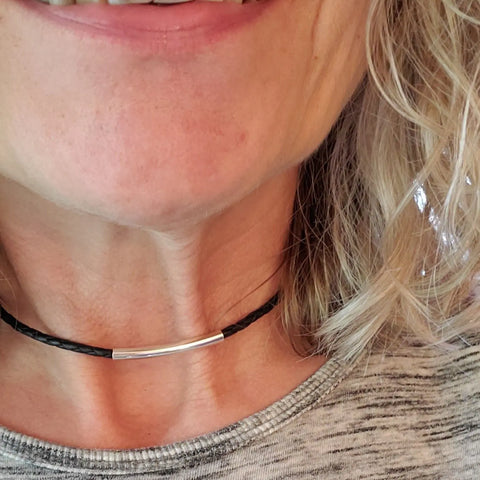 A close-up of a smiling woman with wavy blonde hair and light skin, wearing an Alexa Martha Designs 3mm Bolo Leather Snap Off Choker with a sterling silver tube, paired with a light grey top.