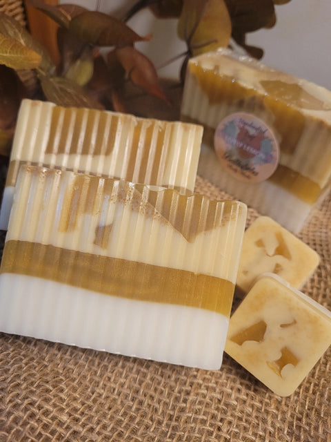 Three striped All Natural Soap Bar - Lively Lemon by Bathsheba Body Works in white and golden yellow rest on burlap, with two small square lemon soaps, decorative leaves, and another natural bar in the background.