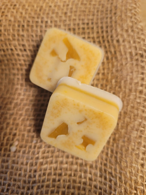 Two square Bathsheba Body Works All Natural Soap Bar – Lively Lemon bars, yellow-and-white marbled with embedded pieces and natural ingredients, rest on coarse brown burlap.