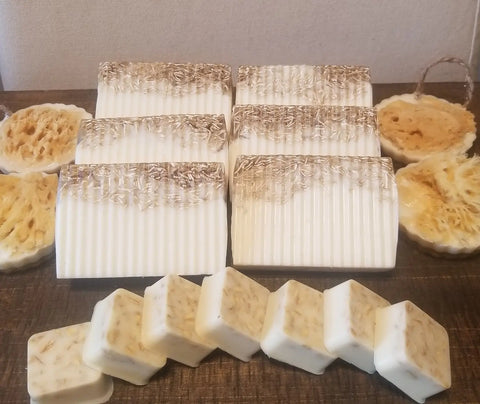 Several Bathsheba Body Works All Natural Soap Bar - Country Life soaps with textured tops, exfoliating loofah slices, and small square pieces with botanical bits are arranged on a wooden surface.