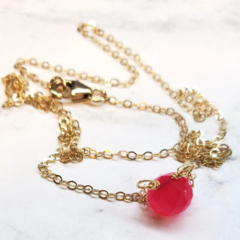The Tiny Hot Pink Chalcedony Gold Filled Necklace by Alexa Martha Designs features a faceted pink chalcedony pendant, elegantly displayed on a white marble surface.