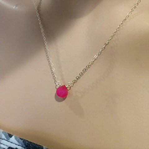 The Tiny Hot Pink Chalcedony Gold Filled Necklace by Alexa Martha Designs features a small teardrop pink stone pendant that rests elegantly on the neck, its beauty enhanced by a softly lit, neutral background.