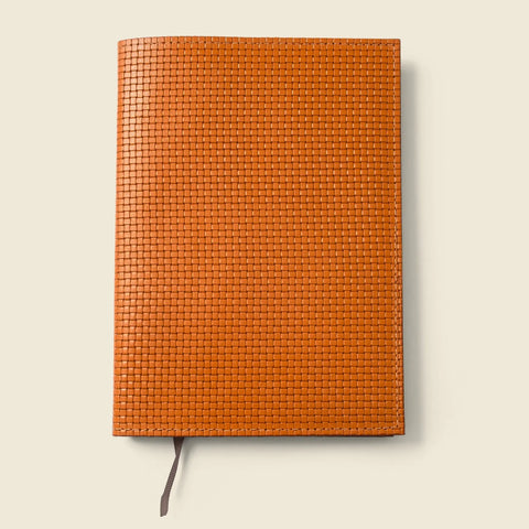 The CASUPO Refillable A5 Leather Notebook Cover – Tan Limited Edition features a textured, woven pattern and brown ribbon bookmark, displayed closed against a light beige background.