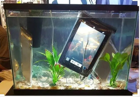 A tablet and a smartphone, each sealed in a LOKSAK ALOKSAK Element Proof Bag 6 x 9, are submerged in a fish tank among rocks and green aquatic plants while the tablet’s camera app shows a photo preview.