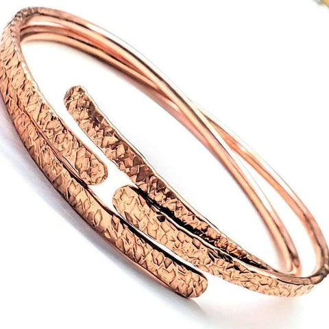 A close-up of the Alexa Martha Designs Adjustable Hammered Copper Overlap Bangle for Him or Her showcases its textured, overlapping surfaces and polished copper bands, highlighting the artistry of this unisex bracelet on a white background.