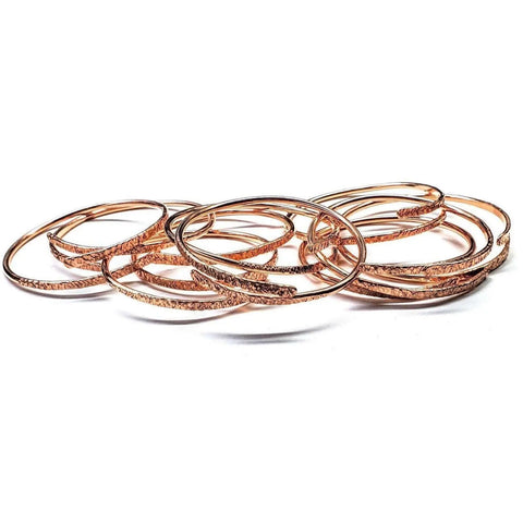 An Adjustable Hammered Copper Overlap Bangle by Alexa Martha Designs for him or her is displayed in a scattered pile on a white background.