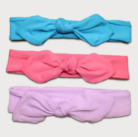 The Goodnighties Knotted Bow Headband 3-Pack features three American-made hair accessories in blue, pink, and lavender. Each headband has a large bow with a similar knot design, arranged vertically from top to bottom.