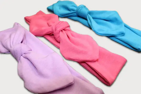 The Goodnighties Knotted Bow Headband 3-Pack features American-made pastel headbands in lavender, pink, and blue, displayed side by side to highlight their charming style.