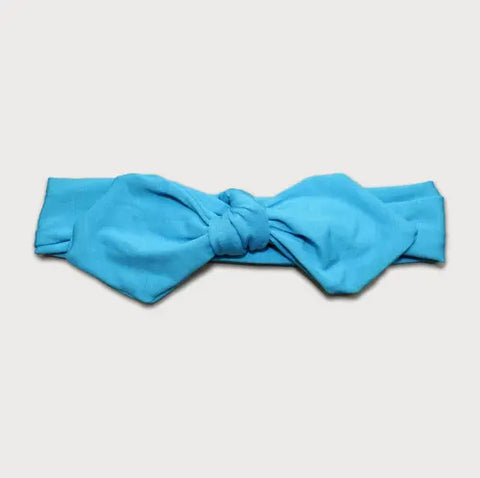 The Goodnighties Knotted Bow Headband is a bright blue, handmade accessory with a central knot and wide bow ends, crafted in the USA and shown on a plain white background.