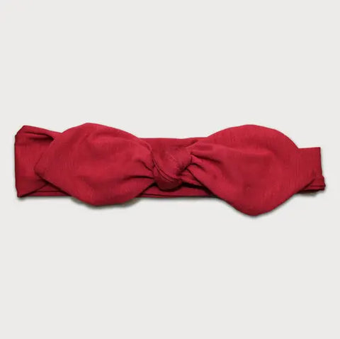 The Goodnighties Knotted Bow Headband is a red, handmade headband featuring a large center knot, shown laid flat on a white background.