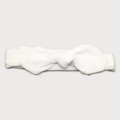The Goodnighties Knotted Bow Headband is a white, handmade accessory from the USA, featuring a large front bow and shown on a plain light gray background.