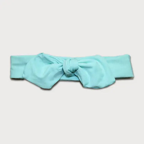 The Goodnighties Knotted Bow Headband is light blue, handmade in the USA, and features a large central bow knot. Shown on a plain white background.