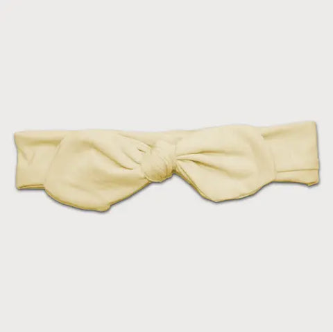 The Goodnighties Knotted Bow Headband features a soft, light yellow fabric with a large central knot and bow, shown on a white background.