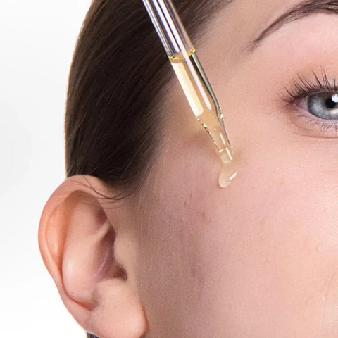 A close-up shows a dropper applying Open Formula Retinoid Serum to a persons cheek near the eye, promoting skin renewal.