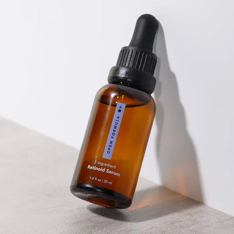 A brown glass dropper bottle labeled Retinoid Serum by Open Formula, 1.0 fl oz / 30 ml, leans against a white surface with a soft shadow—ideal for anti-aging and skin renewal.