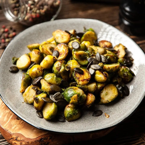 Roasted Brussels sprouts are garnished with pumpkin seeds and finished with Gustus Vitaes Air Fryer Ultimate Veggies Seasoning Set—artisanal spice blends—served on a gray plate atop a wooden board, golden-brown and perfectly seasoned.
