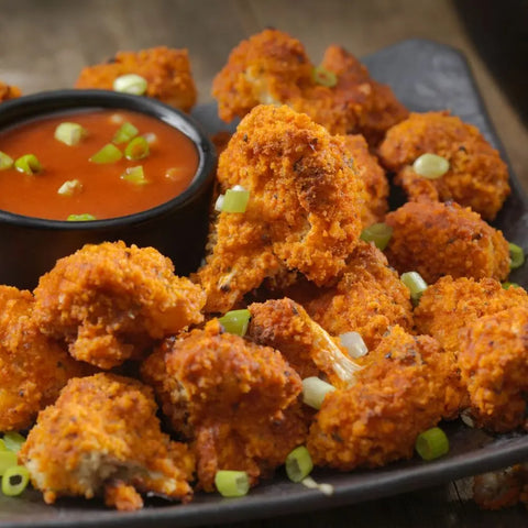 Enjoy crispy buffalo cauliflower bites made with the Gustus Vitae All American Wings Seasoning Set, topped with green onions and served with red dipping sauce—a gourmet take on classic wing flavors.