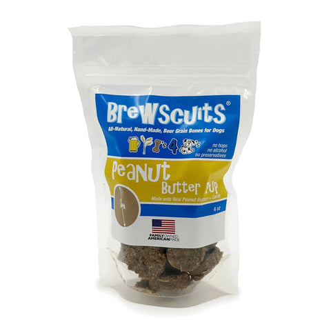 A clear bag of Brewscuits Peanut Butter Pup all-natural dog treats shows the treats inside, with a blue and yellow label featuring sustainable, all-natural ingredients and an American flag.