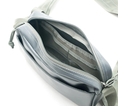 A close-up of the MIS All Weather Shoulder Bag - Foliage shows its open, empty interior and zipper accents. Crafted from vinyl-coated polyester with light gray straps, the crossbody bag is set against a white background.