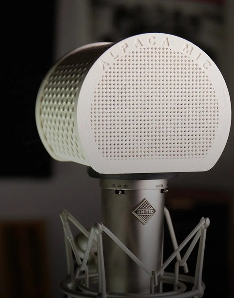 A close-up of the Alpaca Mic, a professional studio condenser microphone with a white perforated windscreen and sleek shock mount. The blurred background emphasizes the premium design and sound quality of this Alpaca Mic product.
