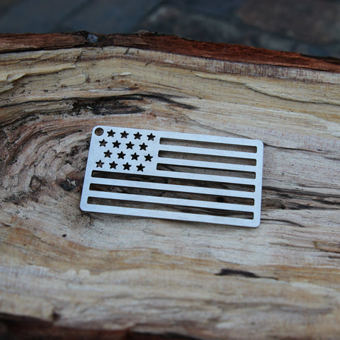 The Arotags American Flag Stainless Steel Key Chain, featuring a U.S. flag design and a hole in the top left corner, is American-made and rests on a textured, weathered wooden surface.