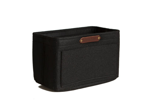 The Urban Southern Tote Insert is a black rectangular lightweight felt basket with structured sides, a front stitched pocket, and a brown leather label on top edge—ideal for customizable organization. Shown against a white background.