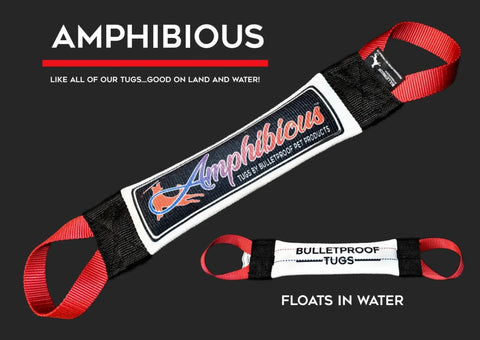 The Amphibious Fire Hose Training Tug by Bulletproof Pet Products Inc is a durable black and white dog toy with red handles, an Amphibious patch, and FLOATS IN WATER”—perfect for play on land or in water!.
