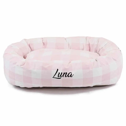 The Majestic Pet Anderson Check Bagel Bed is a soft, oval-shaped dog bed with spine support, a pink and white checkered pattern, and personalized with “Luna” on the front.