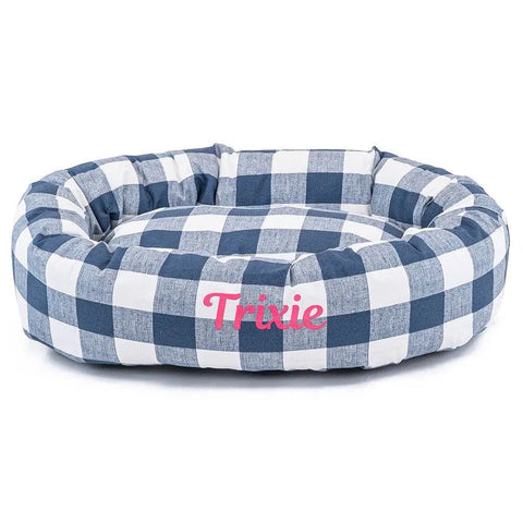 The Majestic Pet Anderson Check Bagel Bed - Personalized features a blue and white checkered design, Trixie in pink letters on the front, and built-in spine support for your pets comfort and relaxation.