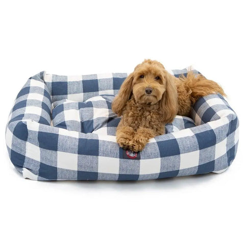 A small brown dog with curly fur relaxes on the Majestic Pet Anderson Check Luxe Bagel Bed in blue and white checks, gazing at the camera.