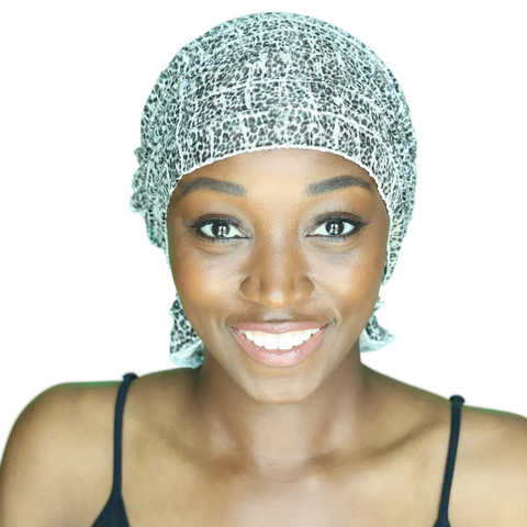 A smiling woman wears a black strap top and the Chemo Beanies® Gina patterned beanie by Chemo Beanies®, looking directly at the camera against a plain background.