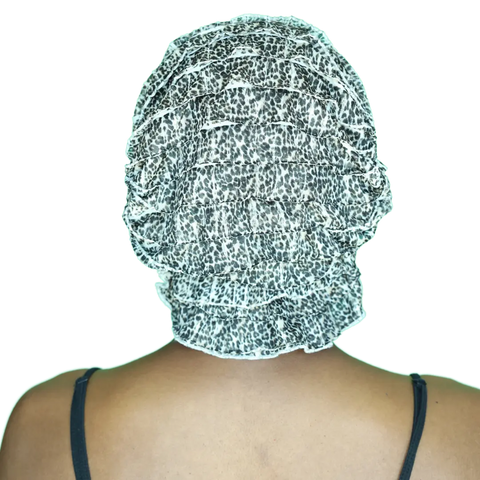 A person faces away from the camera, wearing a thin-strapped dark top with their hair covered by the black and white animal print Chemo Beanies® - Gina cancer headwear bonnet from Chemo Beanies®.