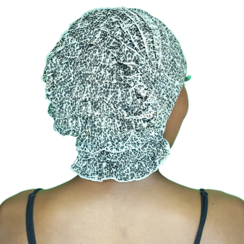 A person is seen from behind wearing the Chemo Beanies® Scarves - Gina, a black and white leopard print slip-on beanie by Chemo Beanies®, commonly used as stylish cancer headwear. Thin black top straps are visible on their shoulders.