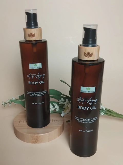 Two brown Forev'Herbs Anti-Aging Body Oil bottles with bamboo pumps sit on a round wooden platform among green leaves and white flowers. These rejuvenating oils promise a youthful glow against a soft beige background.