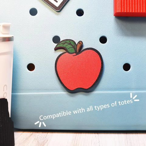 A FRESHe Baglets Teacher Charm (red apple with green leaf) by Chatelet Manufacturing decorates a light blue tote bag. Compatible with all totes including Bogg and Simply Southern—great as a teacher gift or tote accessory.