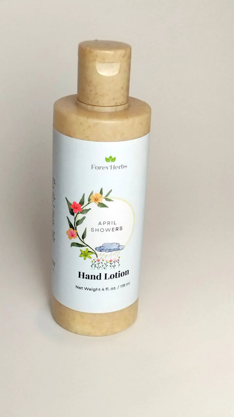 A bottle of Forev'Herbs April Showers Hand Lotion, featuring a floral label, stands upright against a plain light background.