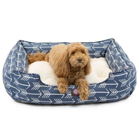 A small, curly-haired brown dog relaxes on the Majestic Pet Arrow Contemporary Lounge Bed, which features soft, cushioned, machine-washable blue sides with a white arrow pattern.