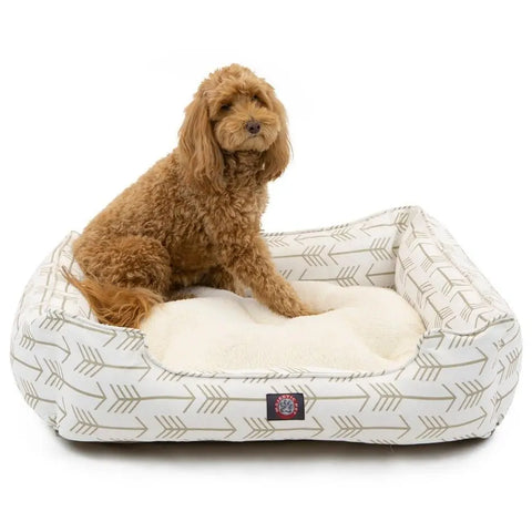 A fluffy brown dog sits on the Majestic Pet Arrow Contemporary Lounge Bed—a white rectangular bed with a beige arrow pattern and a soft cream cushion.