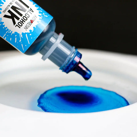 A close-up of ArtResin Alcohol Ink by ArtResin being squeezed onto a white surface, forming a vivid blue pool and dynamic spread—ideal for inspiring resin artists with vibrant color effects.