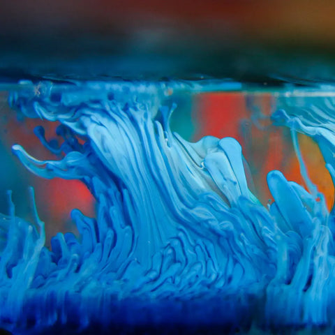 ArtResin Alcohol Ink by ArtResin displays vibrant blue and white swirling patterns, like ocean waves or paint in water, popular with resin artists, set against a blurred background of warm orange and red tones.