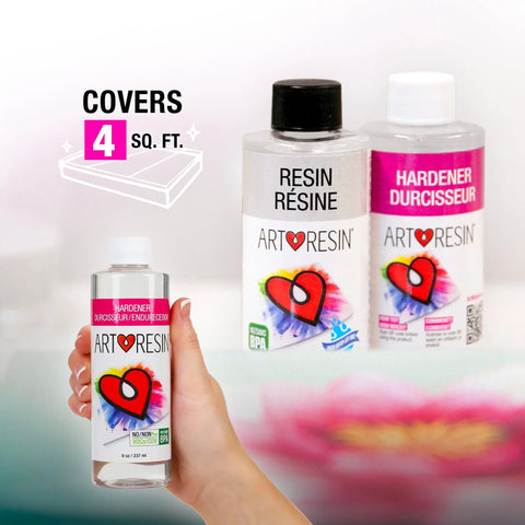 A hand holds a bottle of 16 Oz (474 Ml) ArtResin - Epoxy Resin by ArtResin in front of two labeled bottles. Text reads Covers 4 sq. ft. This non-toxic, professional-grade epoxy resin features a heart on a colorful background.