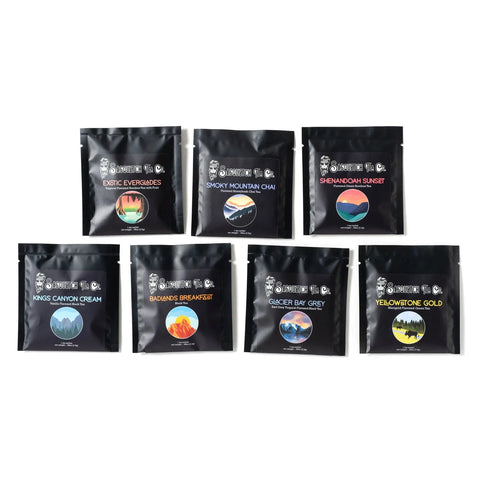 The Son of Sasquatch Tea Sampler by Sasquatch Tea Co features seven black tea packages in two rows, each with a colorful circular label and unique flavors like Exotic Everglades, Smoky Mountain Chai, and Yellowstone Gold.