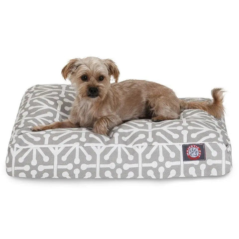 A small brown dog lies on the Majestic Pet Aruba Rectangle Dog Bed, featuring a gray and white geometric pattern, premium polyester fiber fill for extra comfort, and a logo patch in one corner.